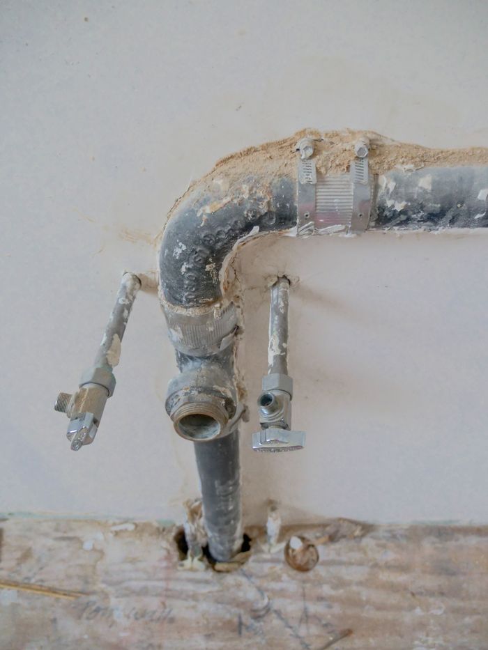 Close-up of exposed plumbing pipes with rustic textures on a construction site wall.